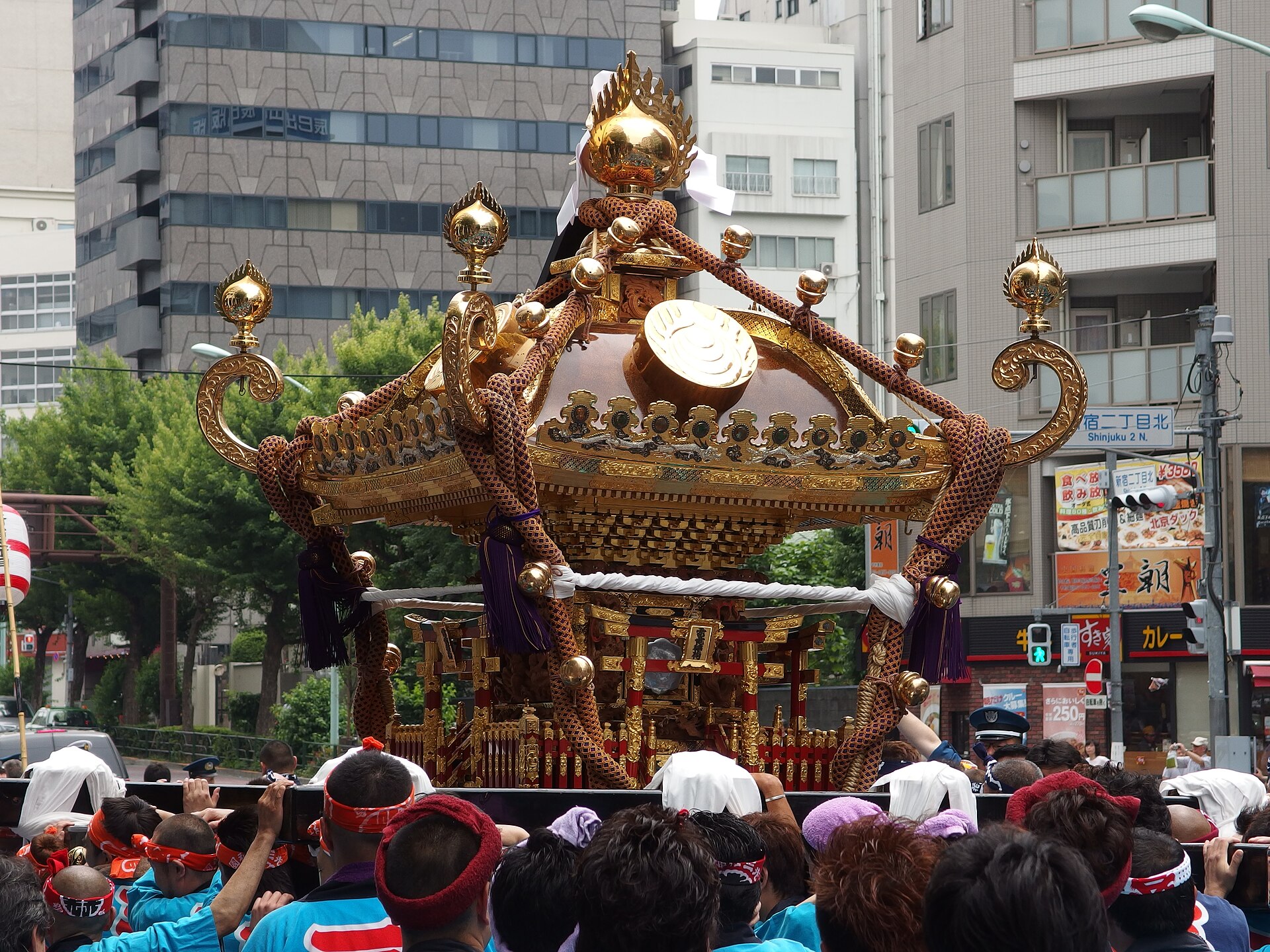 A mikoshi (portable shrine) carried through the streets near Shinjuku 2-chome during the Hanazono Shrine festival. The bearers are seen from behind, with office buildings around them. Photo: Guilhem Vellut / Wikimedia Commons / CC BY 2.0 (25 May 2014)