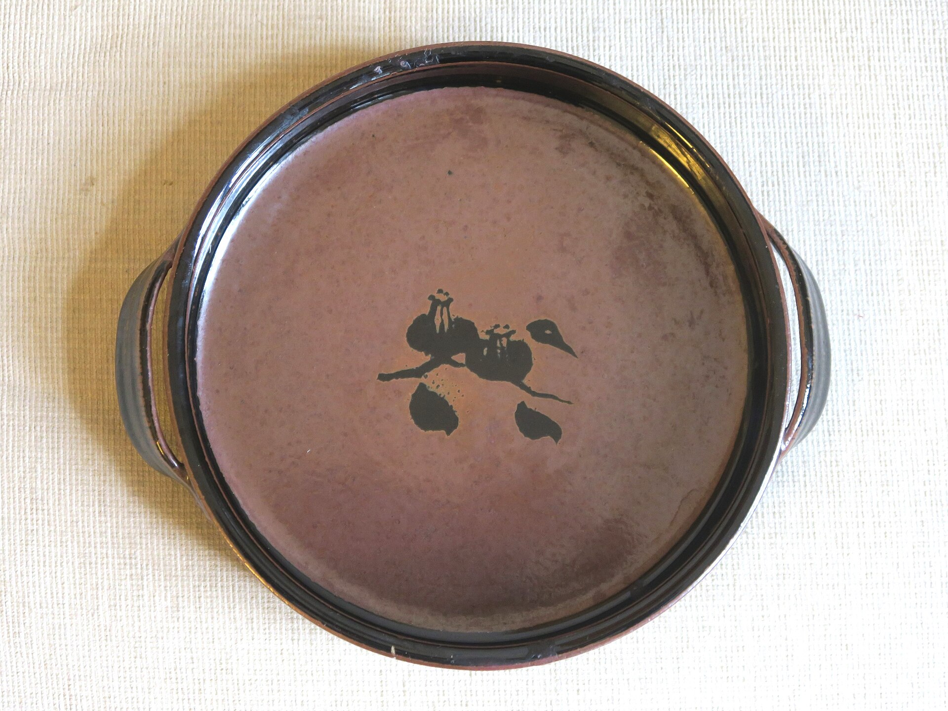 A Mashiko-ware plate with a dark iron glaze and a brushed motif. Photo: Fraxinus2 / Wikimedia Commons / CC BY-SA 4.0