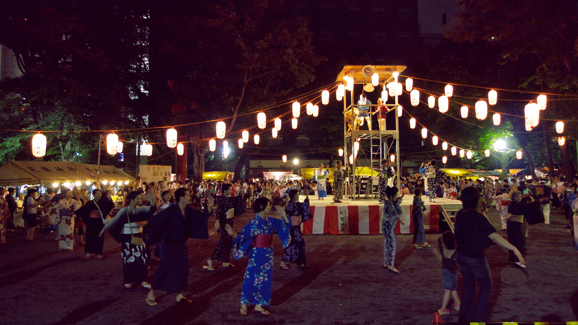 Bon odori at Hanazono Shrine, Shinjuku: people in yukata dance in a circle around the lantern-lit yagura tower. This is a neighbourhood summer festival, not a GCF event. Photo: Yasu / Wikimedia Commons / Public domain (1 August 2009)